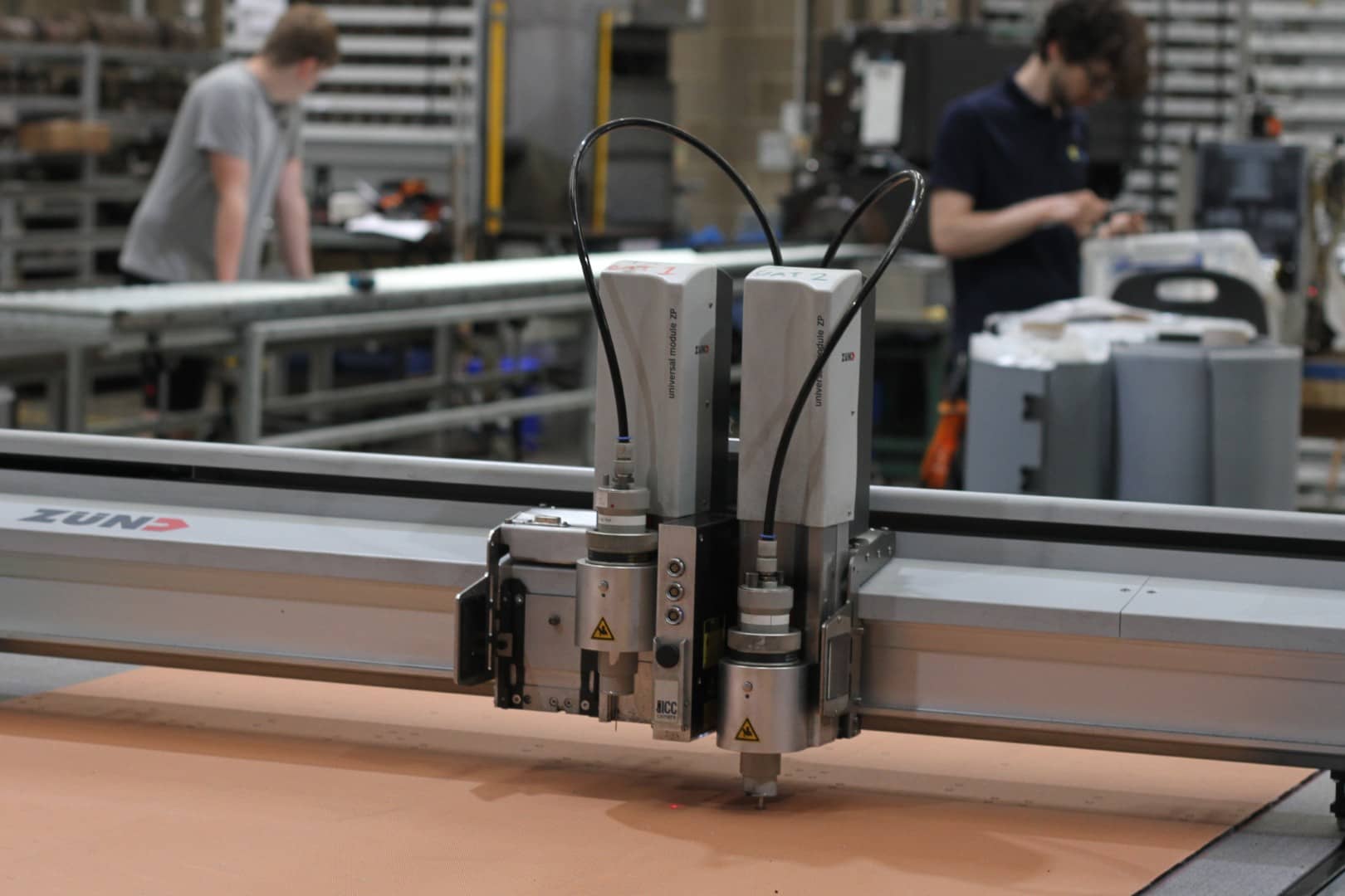 A CNC cutting machine shines a laser on the rubber material on the cutting bed with manufacturing technicians working in the background