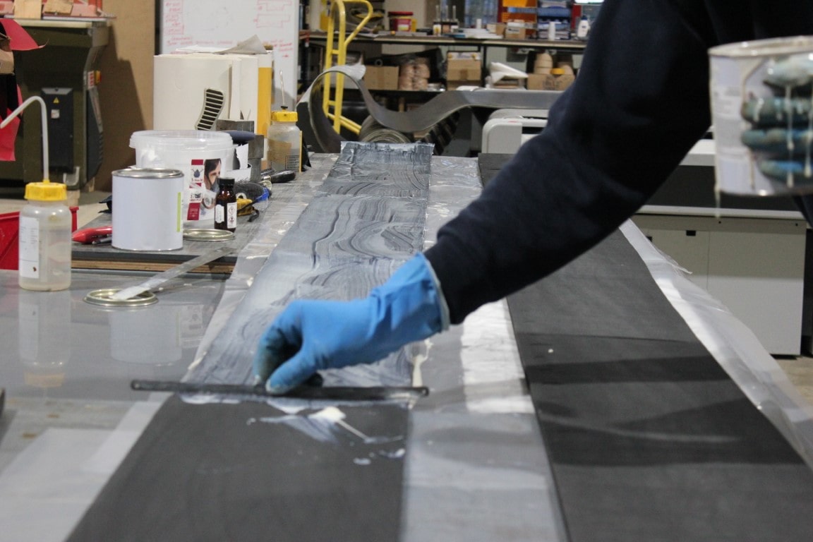 Hand in blue glove spreads white adhesive over a 20cm strip of rubber ready for it to be bonded